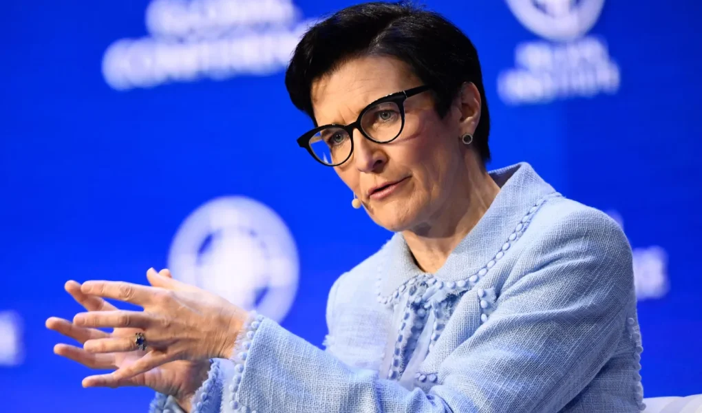 Jane Fraser, CEO of Citigroup, speaking during a panel discussion at a conference. She has short dark hair, wears black-rimmed glasses and a light blue textured jacket, gesturing with her hands against a bright blue background featuring blurred conference branding.