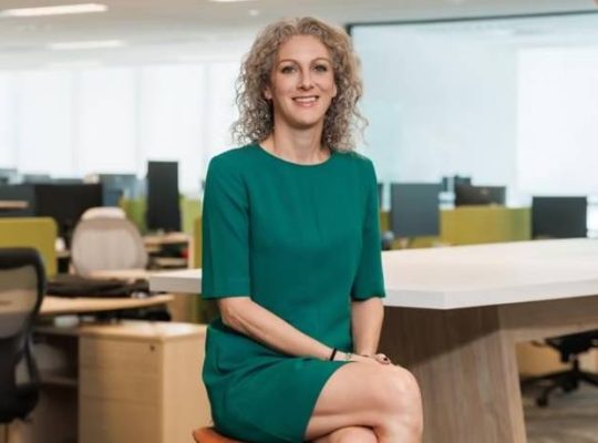 Woman in green dress sitting on poof in office envrionment.