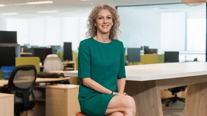 Woman in green dress sitting on poof in office envrionment.
