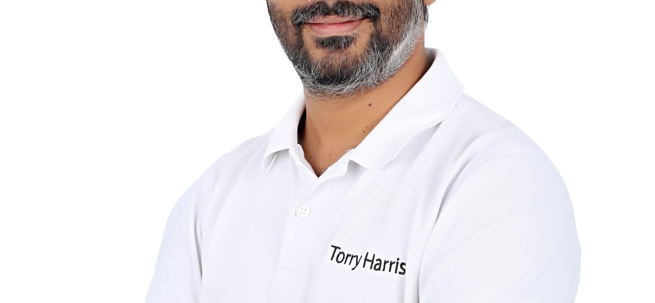 Corporate headshot of a Torry Harris employee, smiling with arms crossed against a white background.
