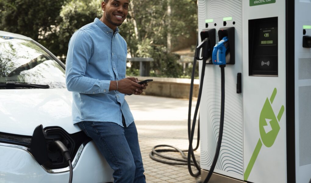 A man charges a white electric vehicle at a public EV charging station