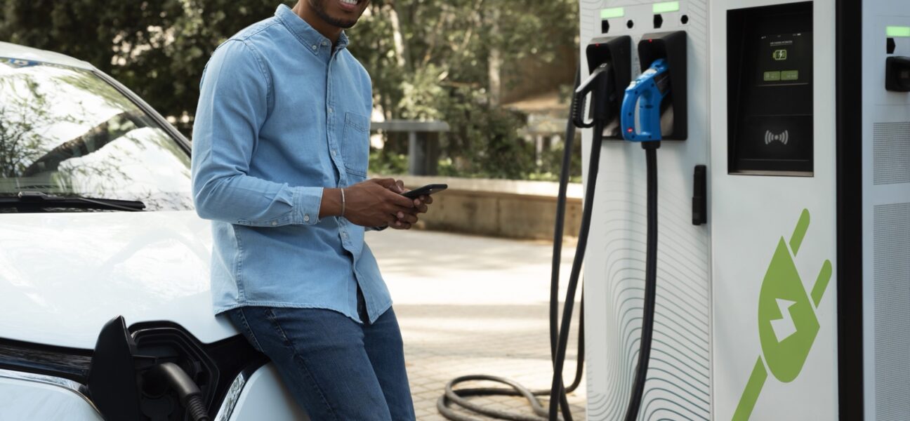 A man charges a white electric vehicle at a public EV charging station