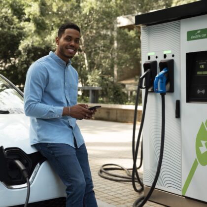 A man charges a white electric vehicle at a public EV charging station