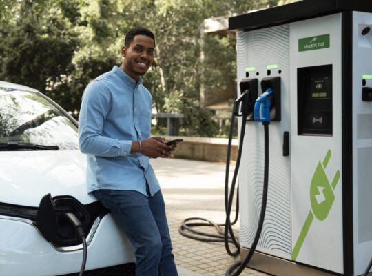 A man charges a white electric vehicle at a public EV charging station