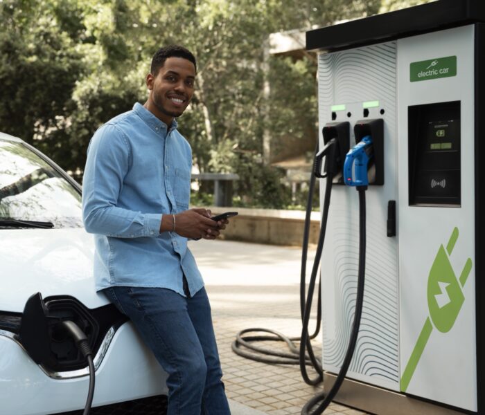 A man charges a white electric vehicle at a public EV charging station