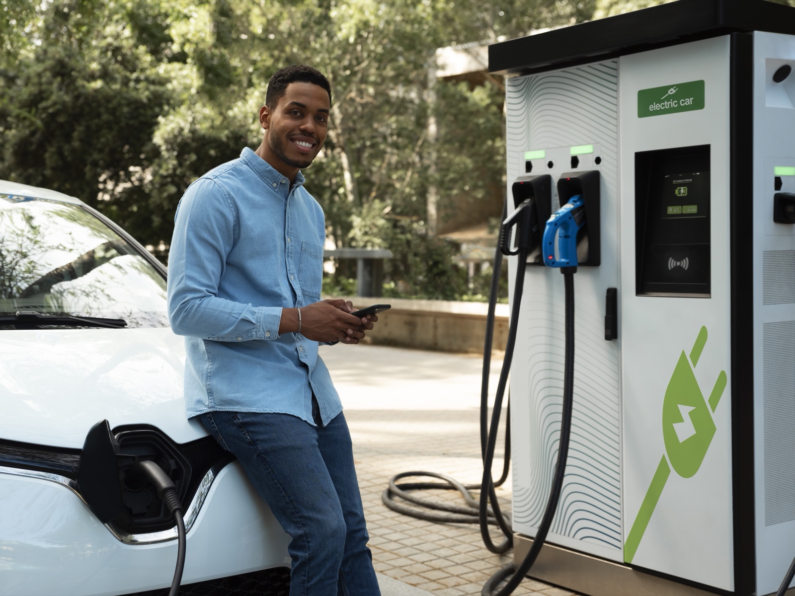 A man charges a white electric vehicle at a public EV charging station